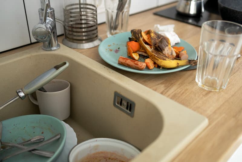 A view of a dirty kitchen sink, with lots of food scraps and used plates