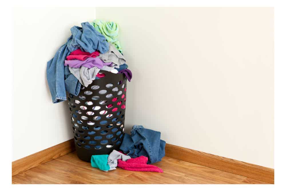 A pile of dirty unwashed laundry in a hamper in the corner of someones bedroom