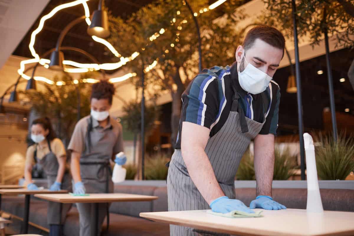 A team of restaurant staff are cleaning restaurant tables before opening